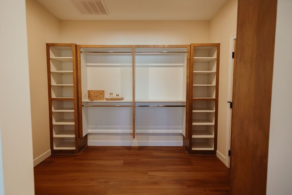 Walk-in closet with wooden shelves, hanging rods, and hardwood floors. White and brown color scheme.