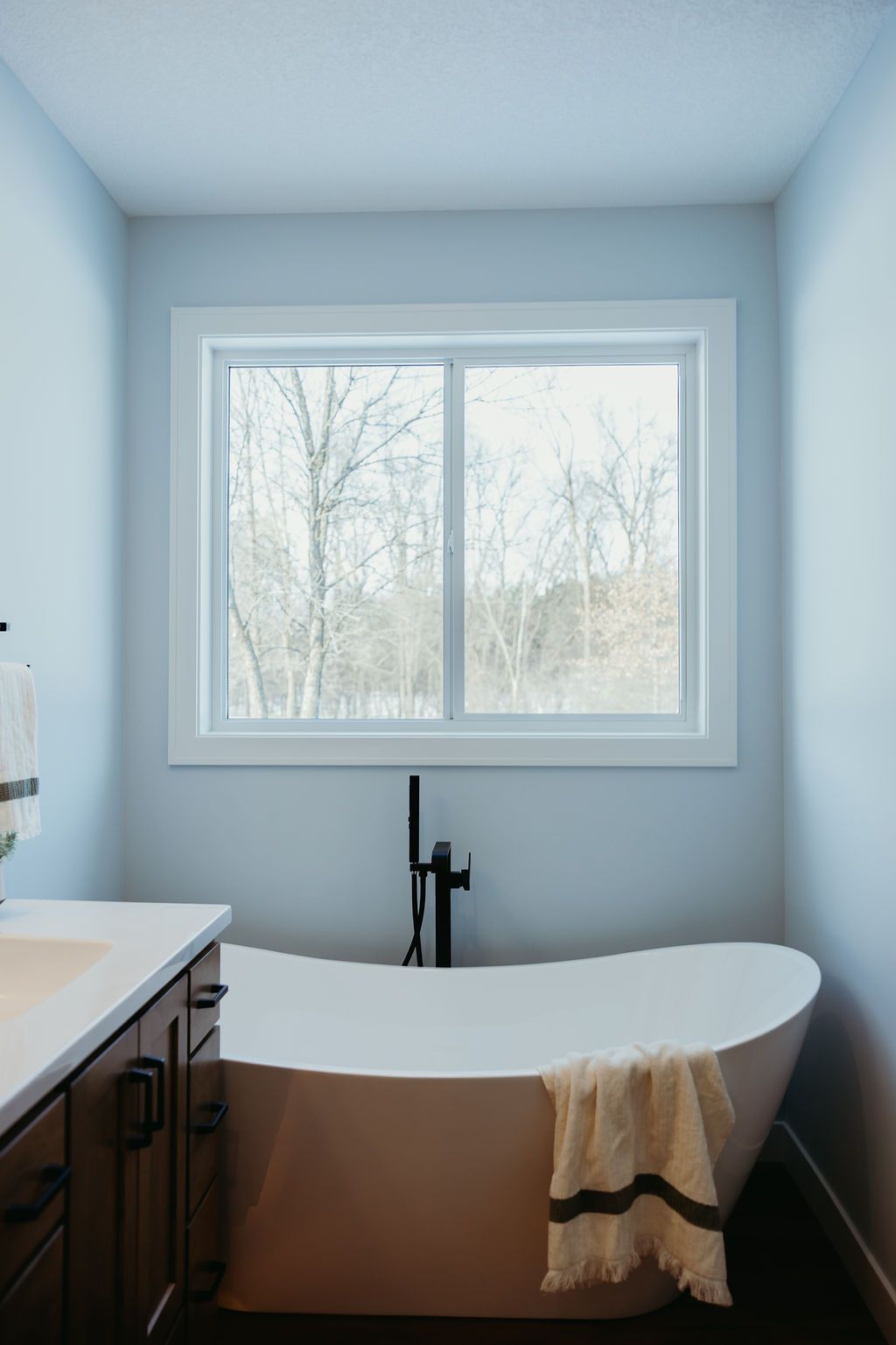 Bathroom with a white freestanding tub, black faucet, and window overlooking trees.