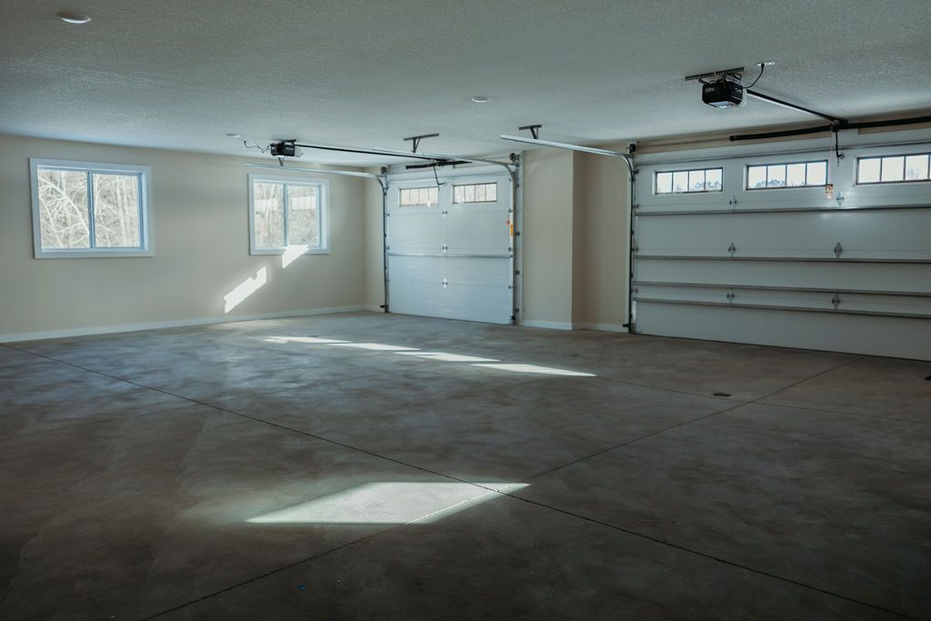 Empty garage with two closed doors, concrete floor, and two windows.