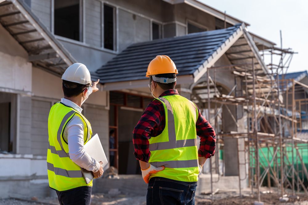 Two construction workers in hard hats and safety vests inspecting a house under construction