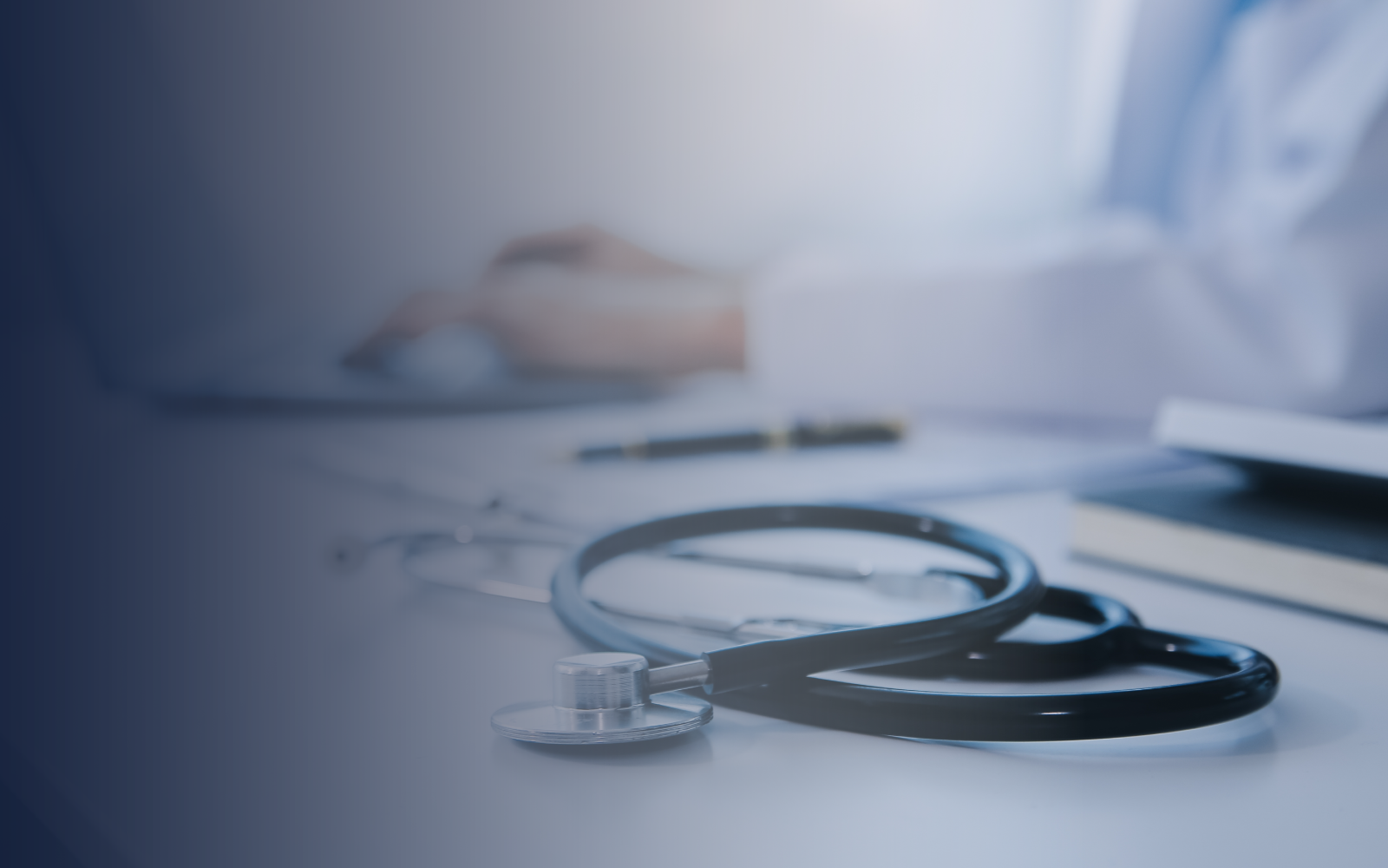 Stethoscope on a desk with papers, a book, and a doctor in the background. Blue and white tones.