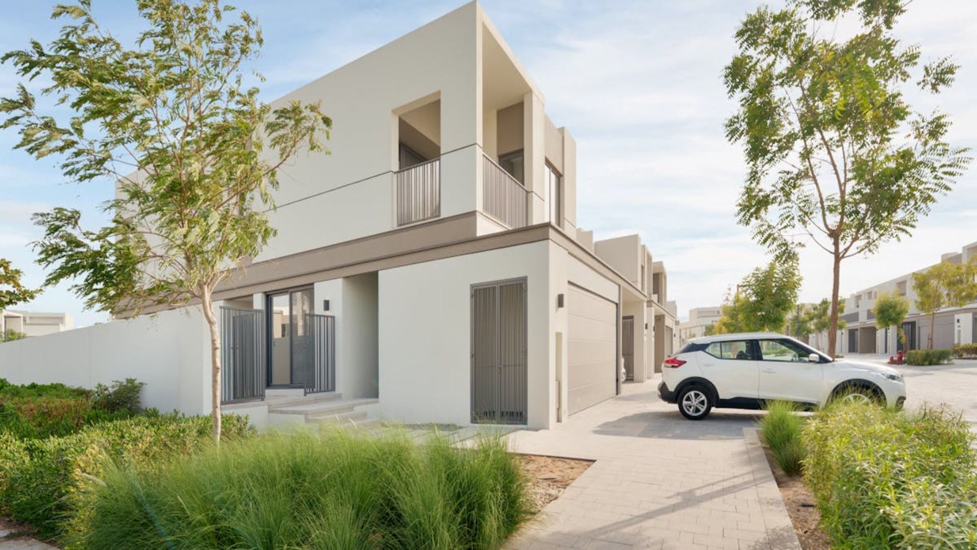 Modernas casas adosadas de dos plantas con exteriores en tonos claros. Un coche blanco está aparcado en la entrada.