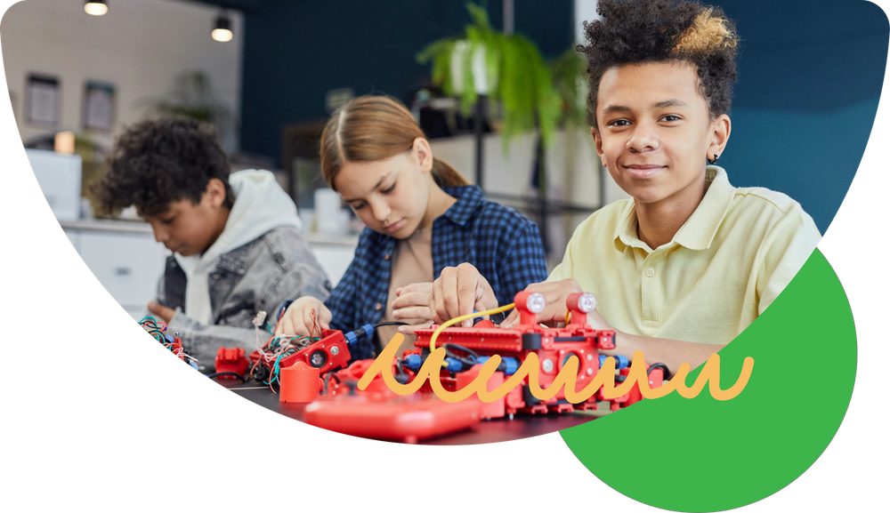 Three diverse kids build a red robot in a classroom, smiling with focus.