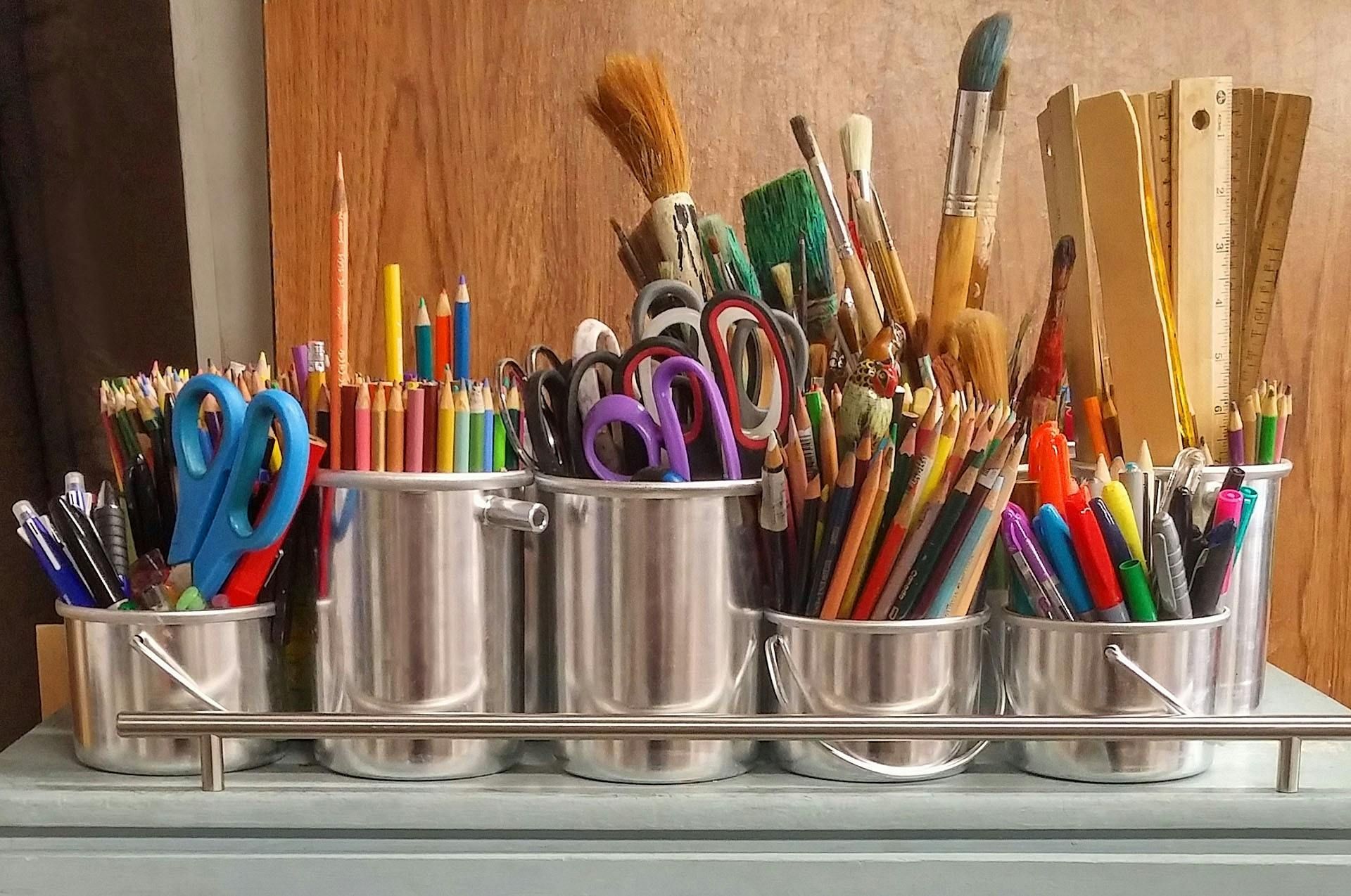 Collection of art supplies in metal containers: pencils, scissors, paintbrushes, rulers.