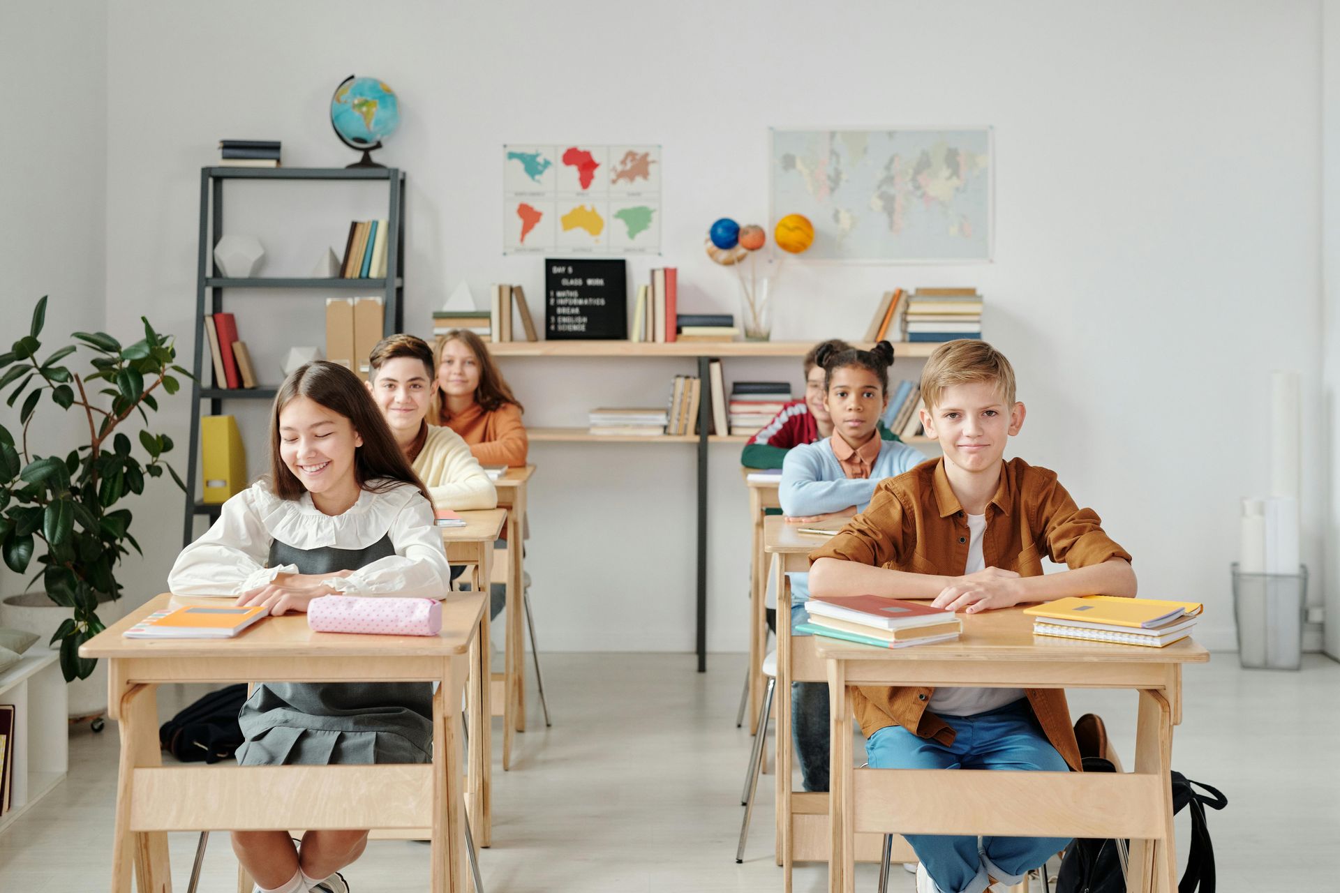 Students seated at desks in a classroom, smiling at the camera.