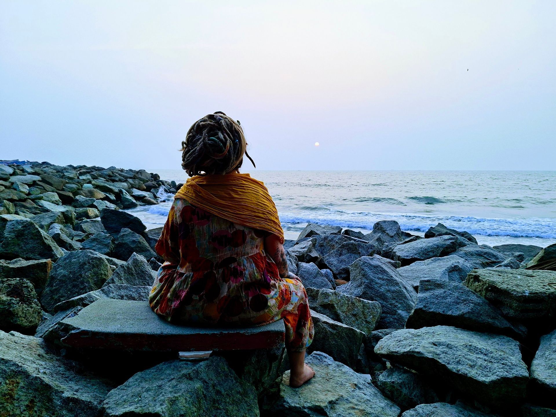 Vrouw zit in meditatie met haar rug naar de camera, uitkijkend over de zee, symbool voor stilte, toe