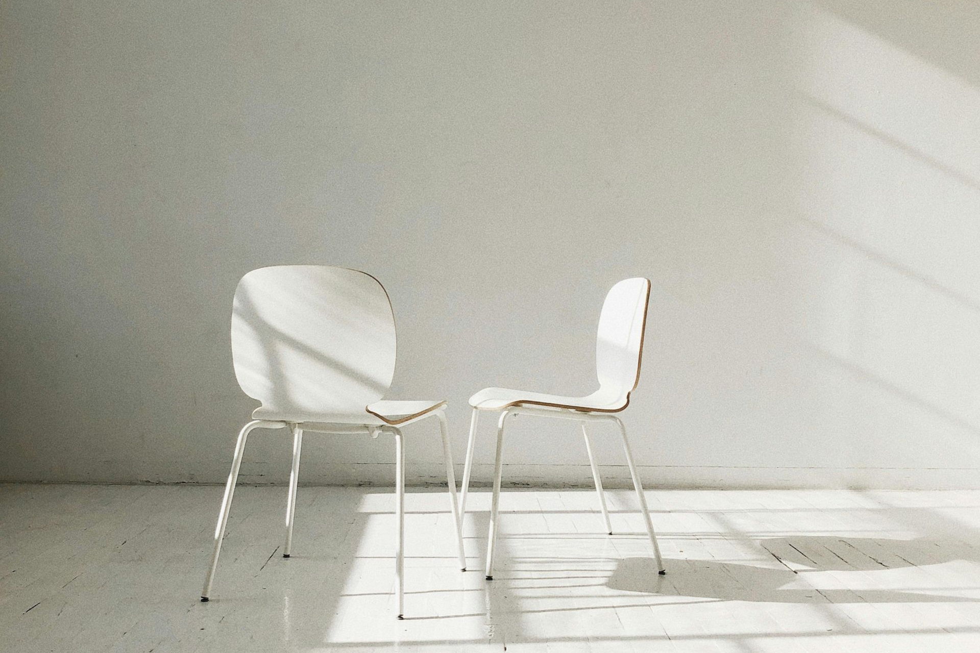 Twee lege stoelen in zacht licht; hun schaduwen raken elkaar op de vloer