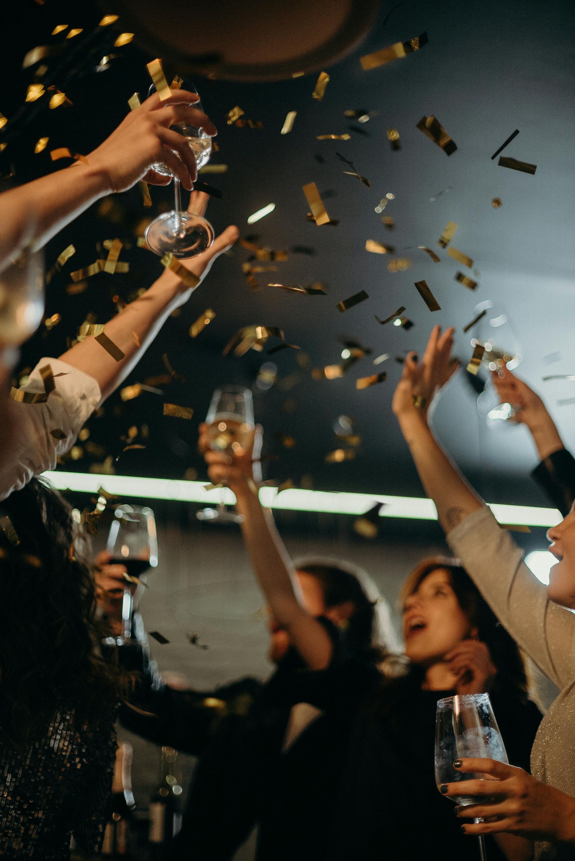 People celebrating with champagne, confetti falling; dark setting, arms raised.