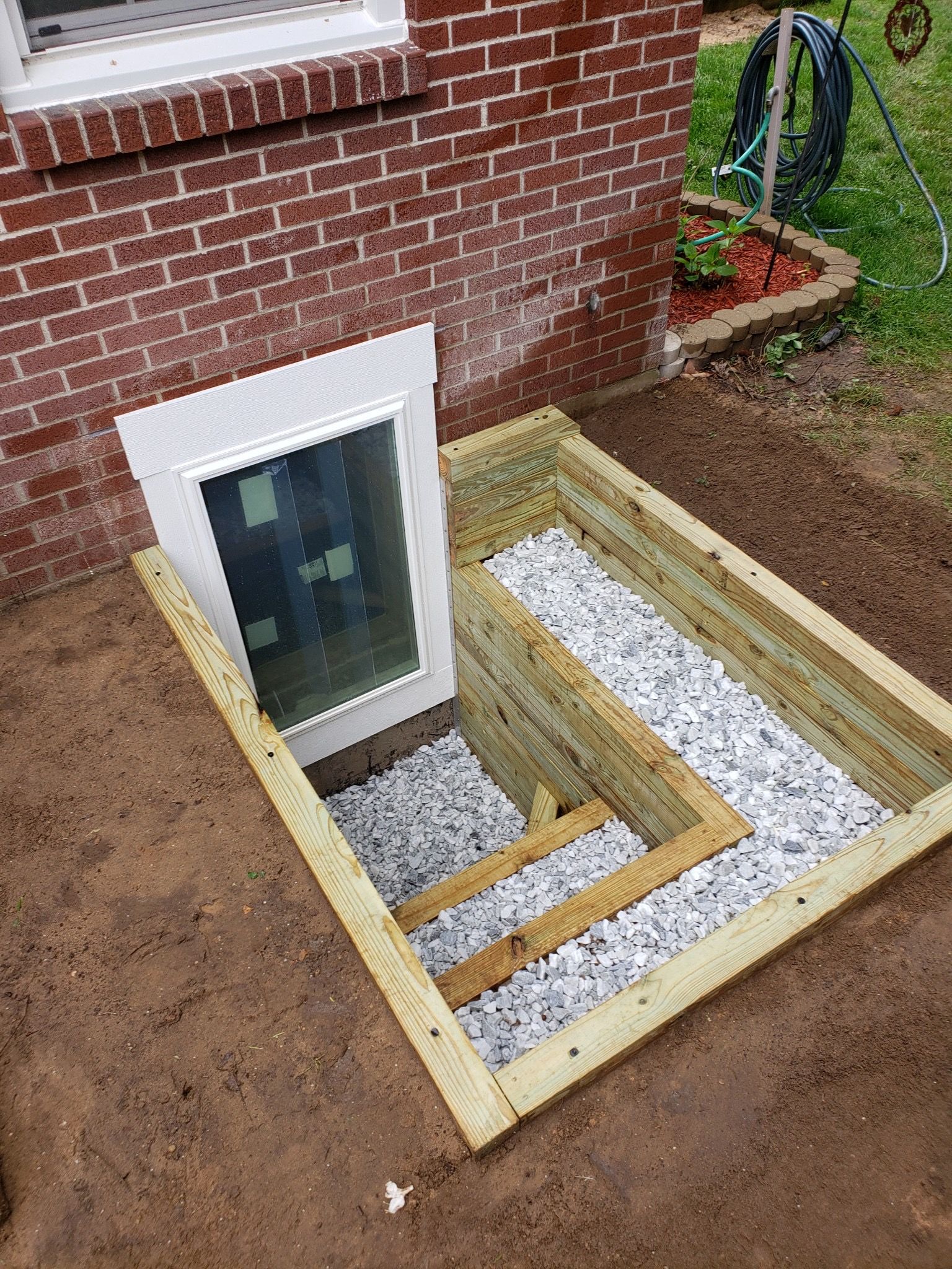 A window well is being built in the ground next to a brick building.