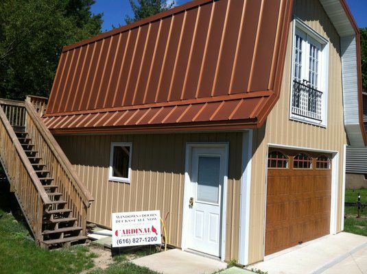 Two-story building with a copper roof, tan siding, garage door, and wooden staircase.