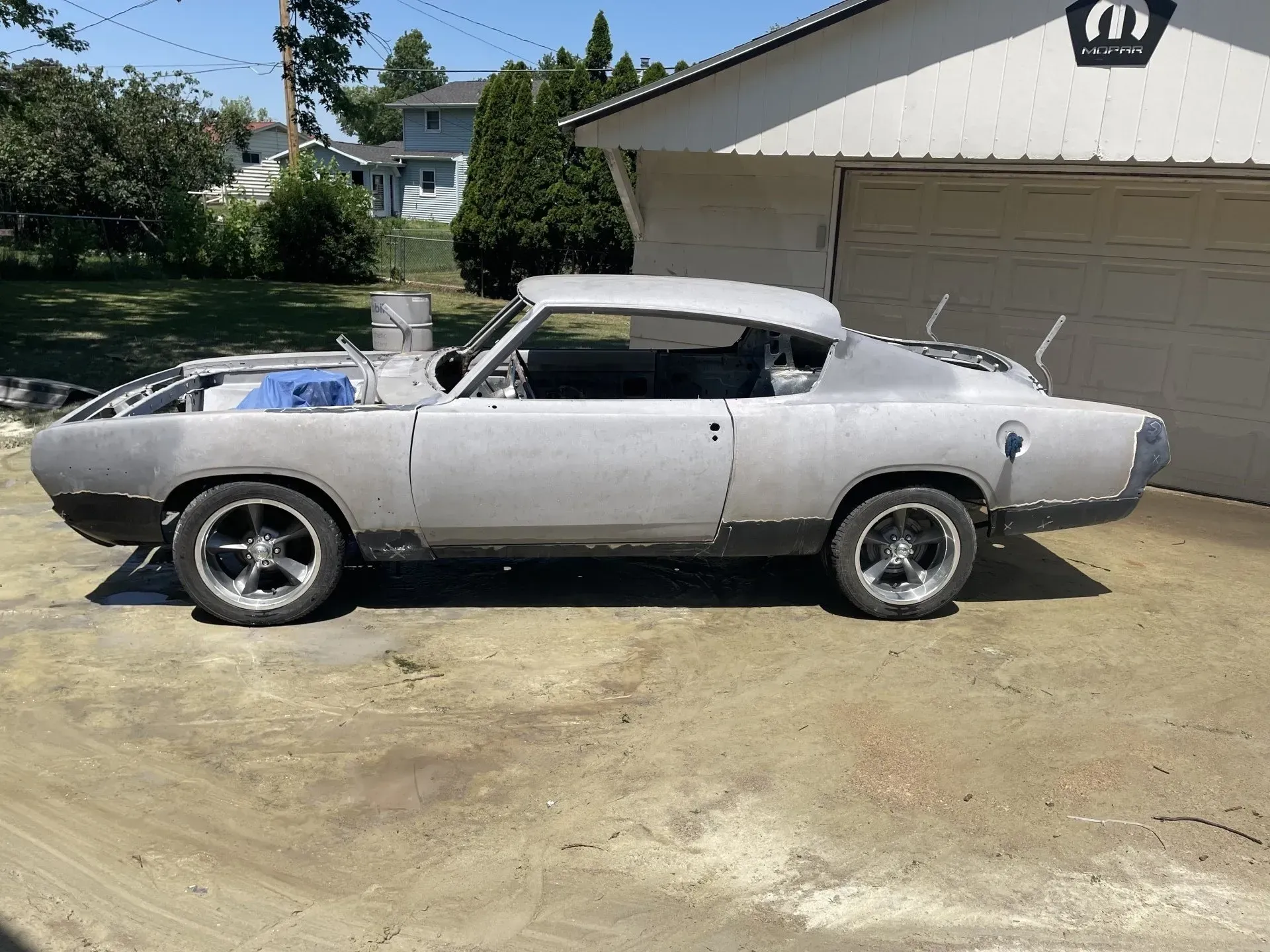A stripped, primer-gray vintage car body mounted on a metal shop stand outside a building.