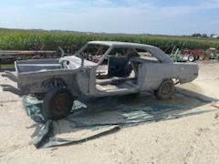 A stripped, primer-gray vintage car body mounted on a metal shop stand outside a building.