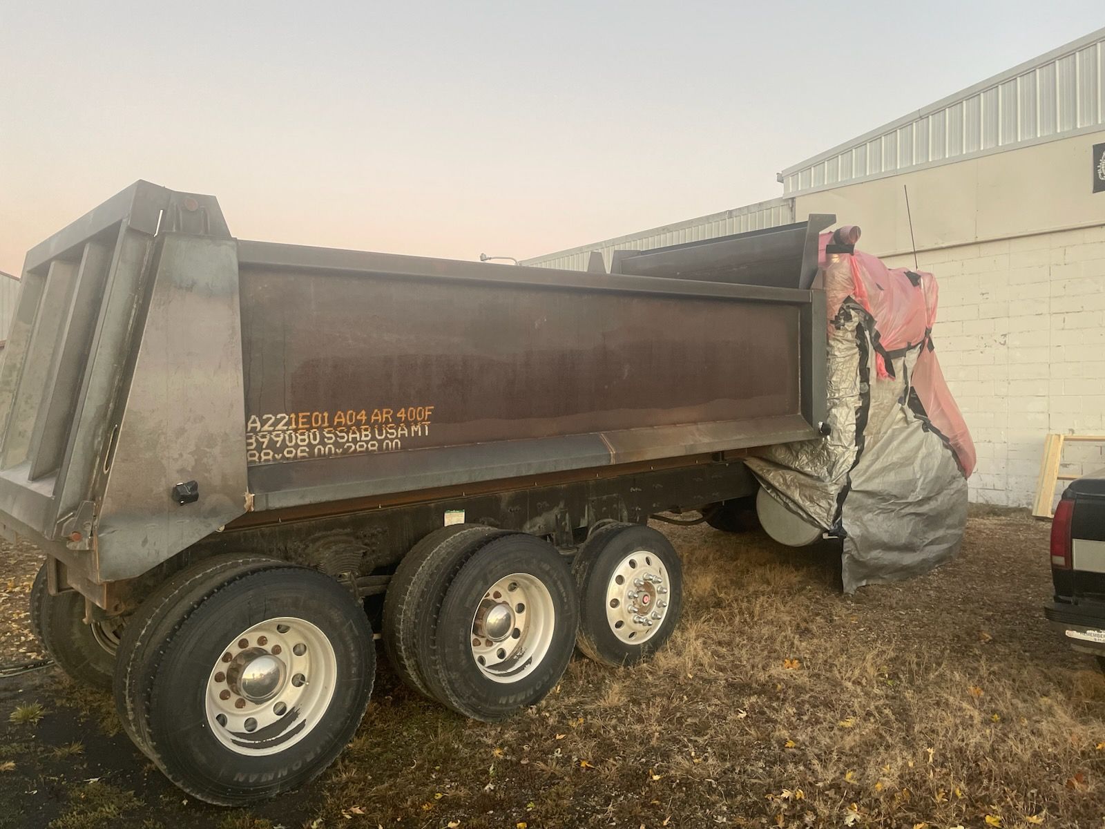 A red heavy-duty lowboy trailer parked on a dirt lot under a cloudy sky.