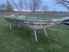 A green, flat-bottomed aluminum utility boat sitting on metal sawhorses in a grassy field at dusk.