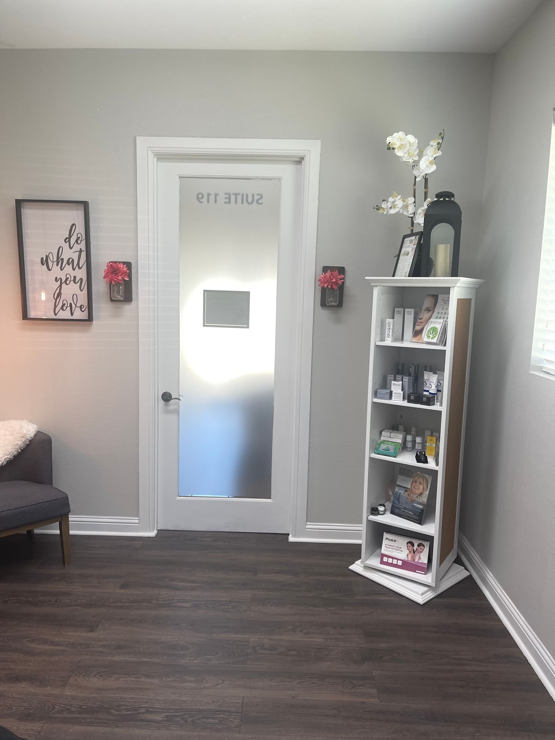 A waiting area with gray walls, a door with frosted glass, and a white bookshelf displaying products.