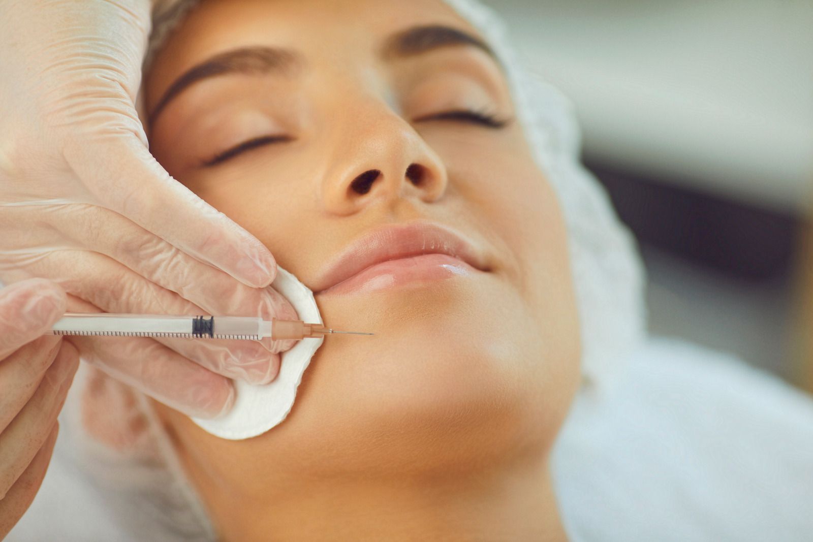 Woman receiving lip filler injection. A gloved hand holds a syringe near her lip.