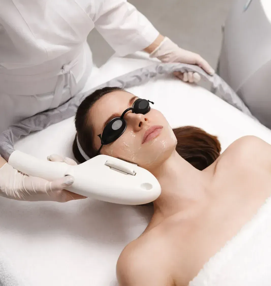 A woman wearing sunglasses is getting a laser treatment on her face