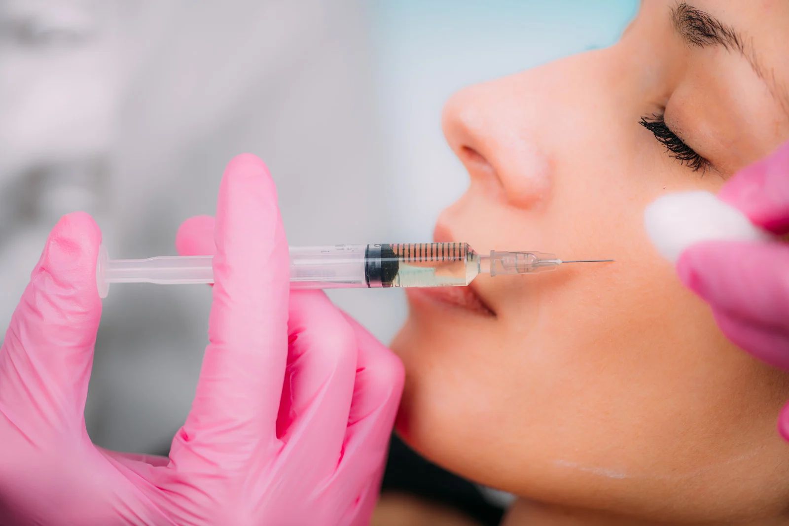 Person receiving lip filler injection. Pink gloves hold syringe near the mouth.