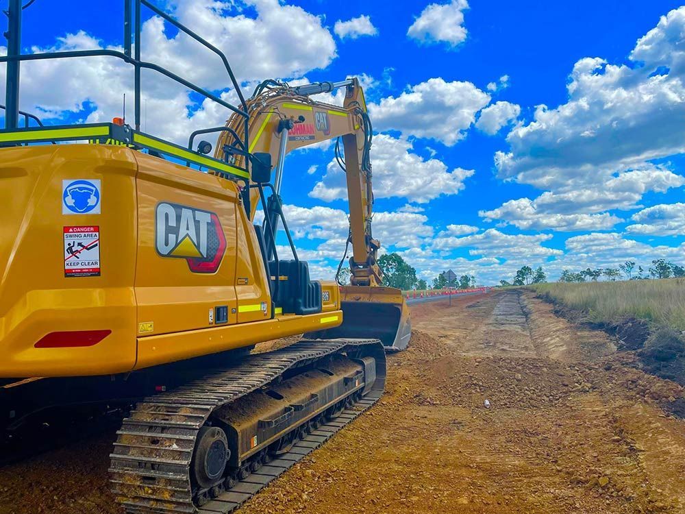 A Yellow Cat Excavator is Parked on the Side of a Dirt Road — Lohman Contracting in Emerald, QLD