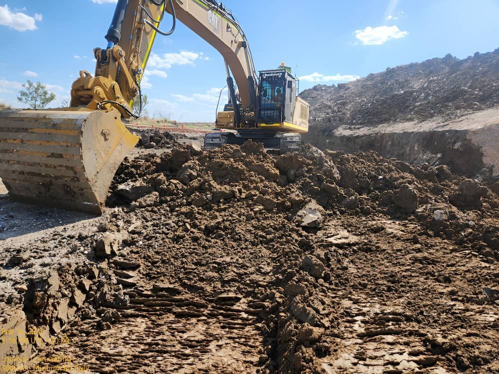 A Large Excavator Is Moving Dirt In A Muddy Field — Lohman Contracting in Charters Towers, QLD