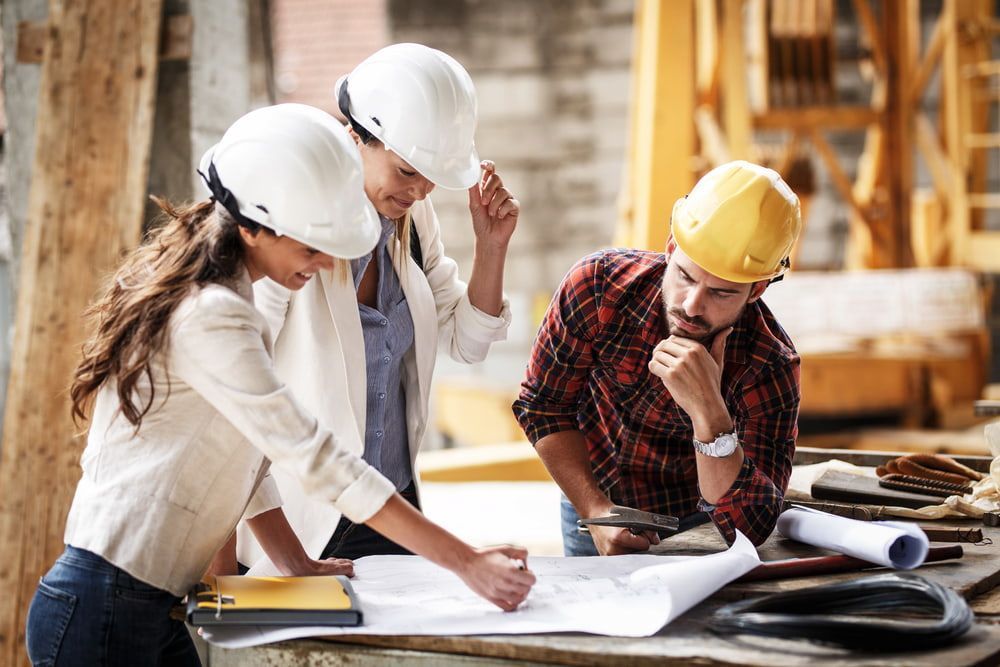 A Group Of Construction Workers Are Looking At A Blueprint At A Construction Site — Lohman Contracting in Emerald, QLD
