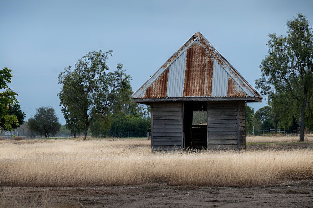 An Old Wooden Building With A Rusty Tin Roof Is Sitting In The Middle Of A Field — Lohman Contracting in Biloela, QLD