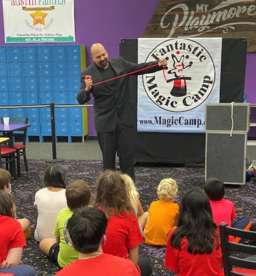 a man is performing a trick in front of a fantastic magic camp sign