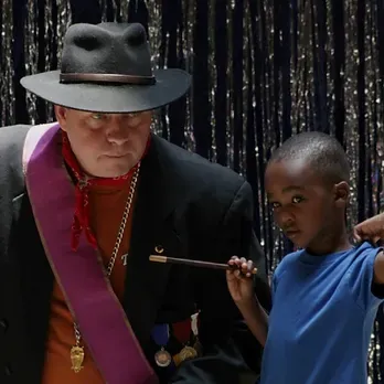 A man in a hat is holding a wand next to a boy in a blue shirt