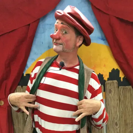 A man wearing a red hat and striped shirt is standing in front of a red curtain