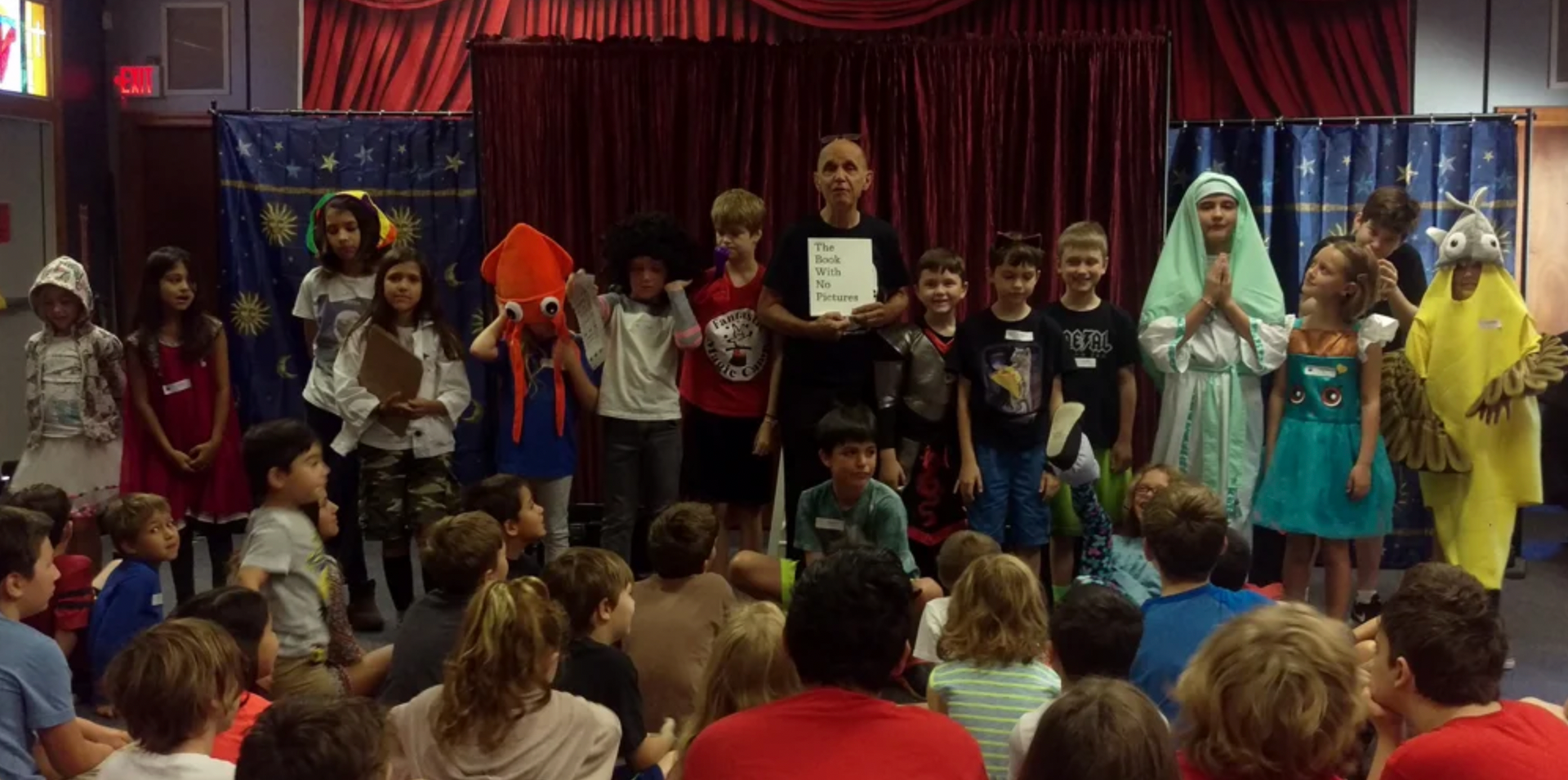 a group of children are standing on a stage in front of a crowd .