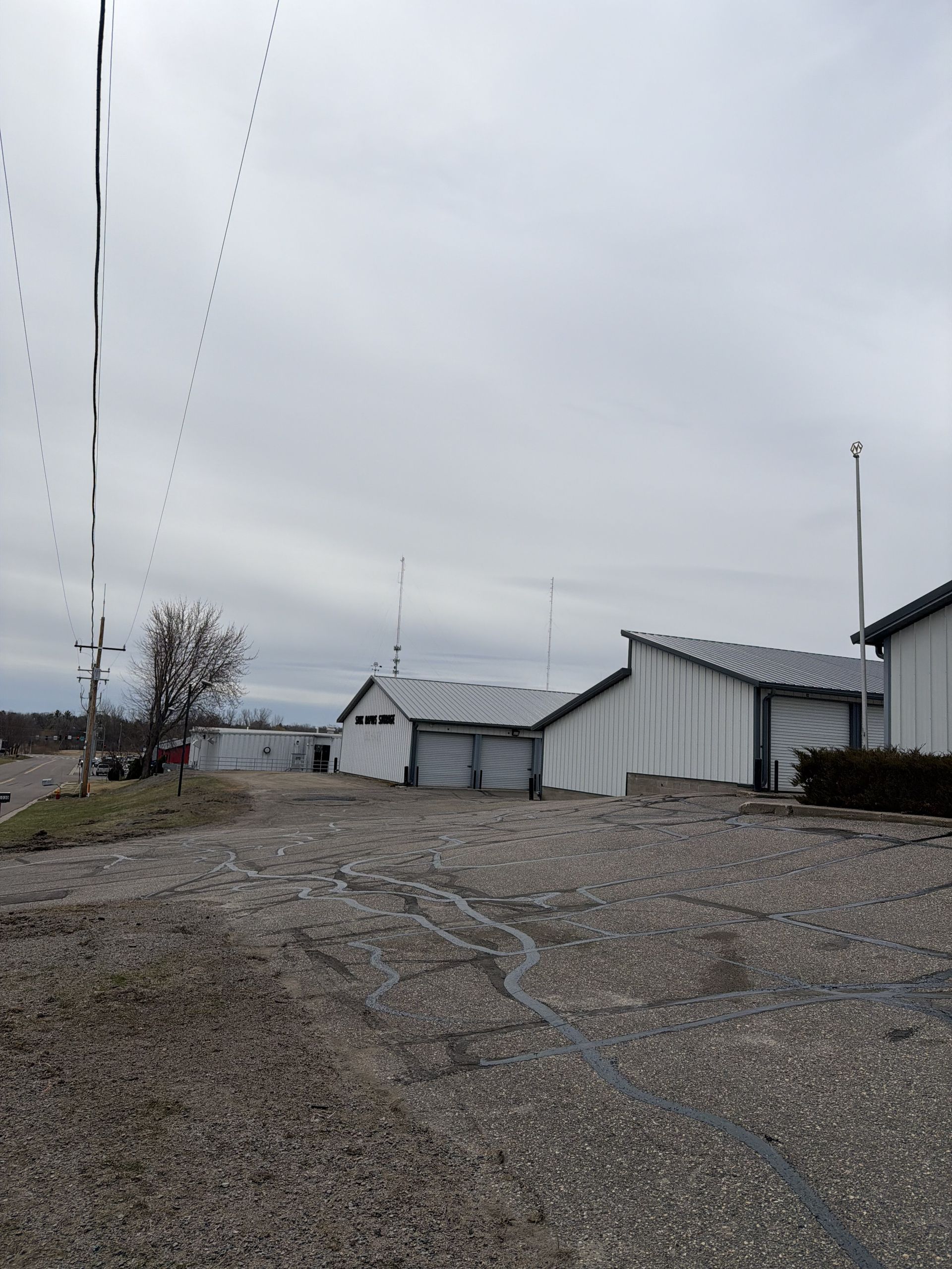 Gravel yard with white buildings and utility poles under a gray overcast sky