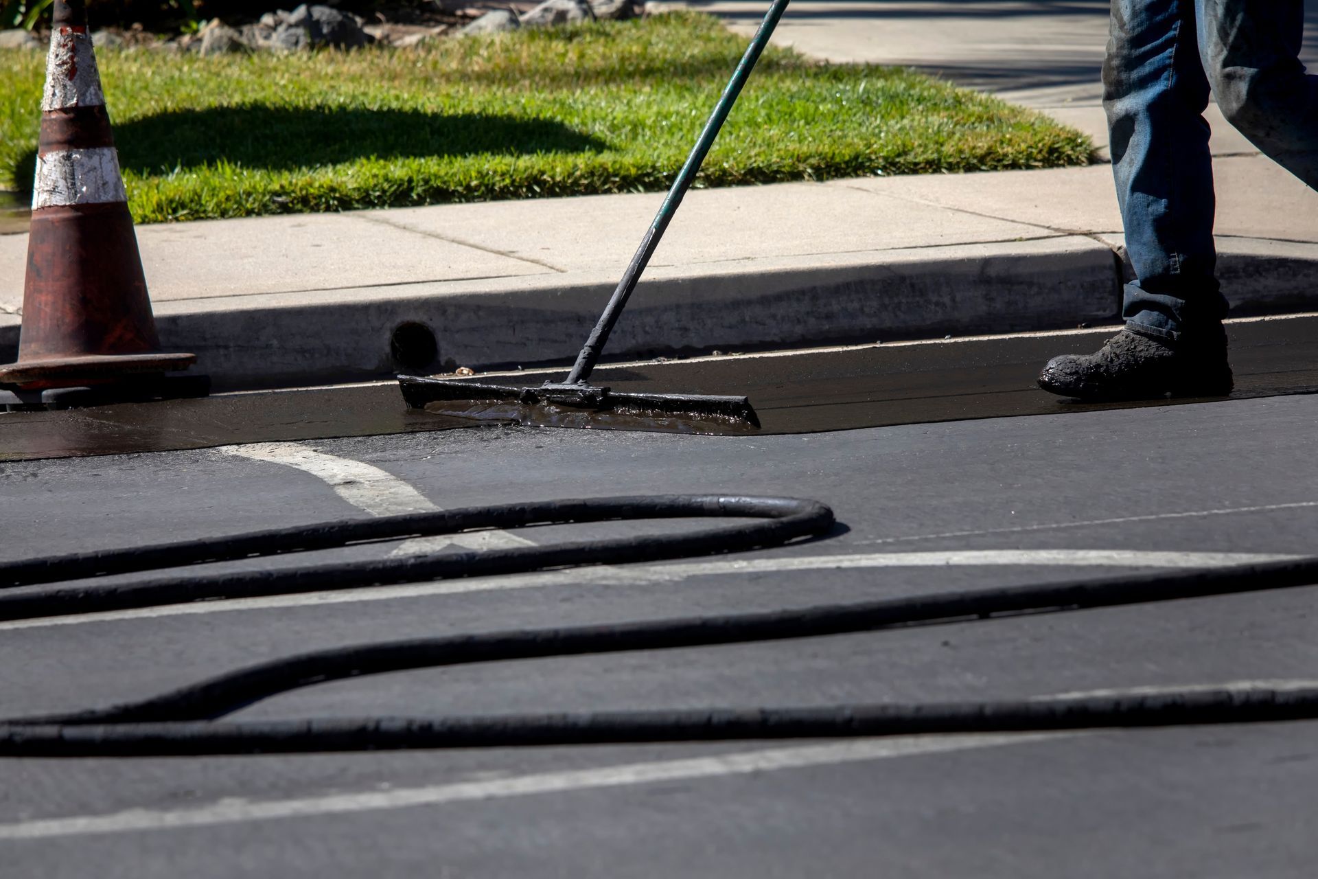 Road workers sweeping debris from a street near an orange cone and curb
