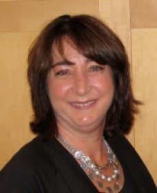 A woman wearing a black shirt and a silver necklace smiles for the camera.