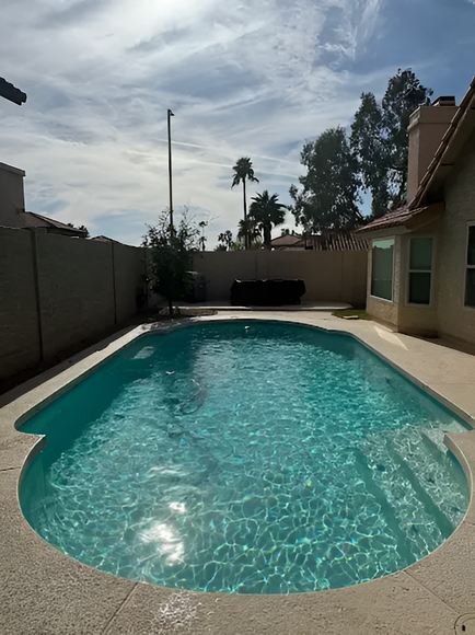 A backyard with a swimming pool, sunny day, and clear blue water.  Walls and house in the background.