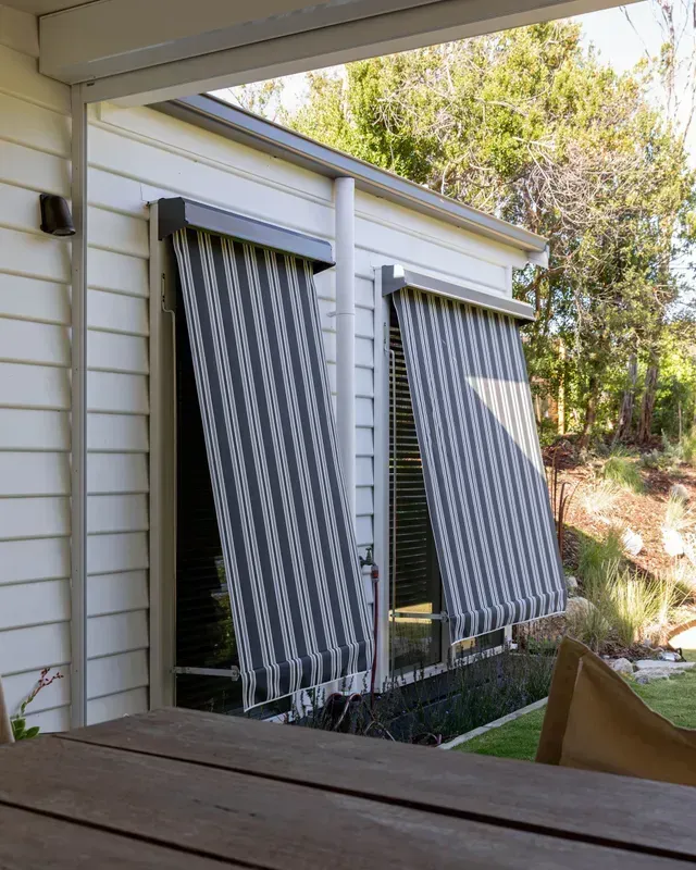 Exterior view of a building with two windows covered by striped roller blinds, partially rolled down.
