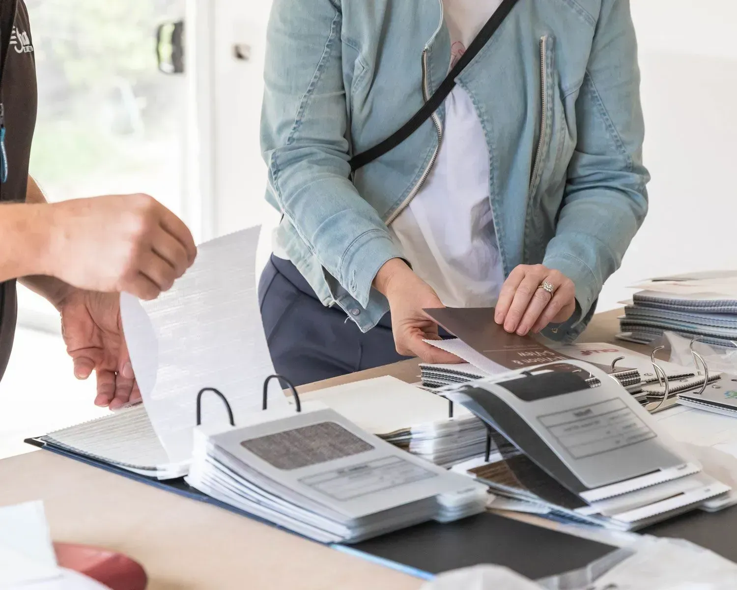 People looking at papers and folders on a table, in a light-filled room.