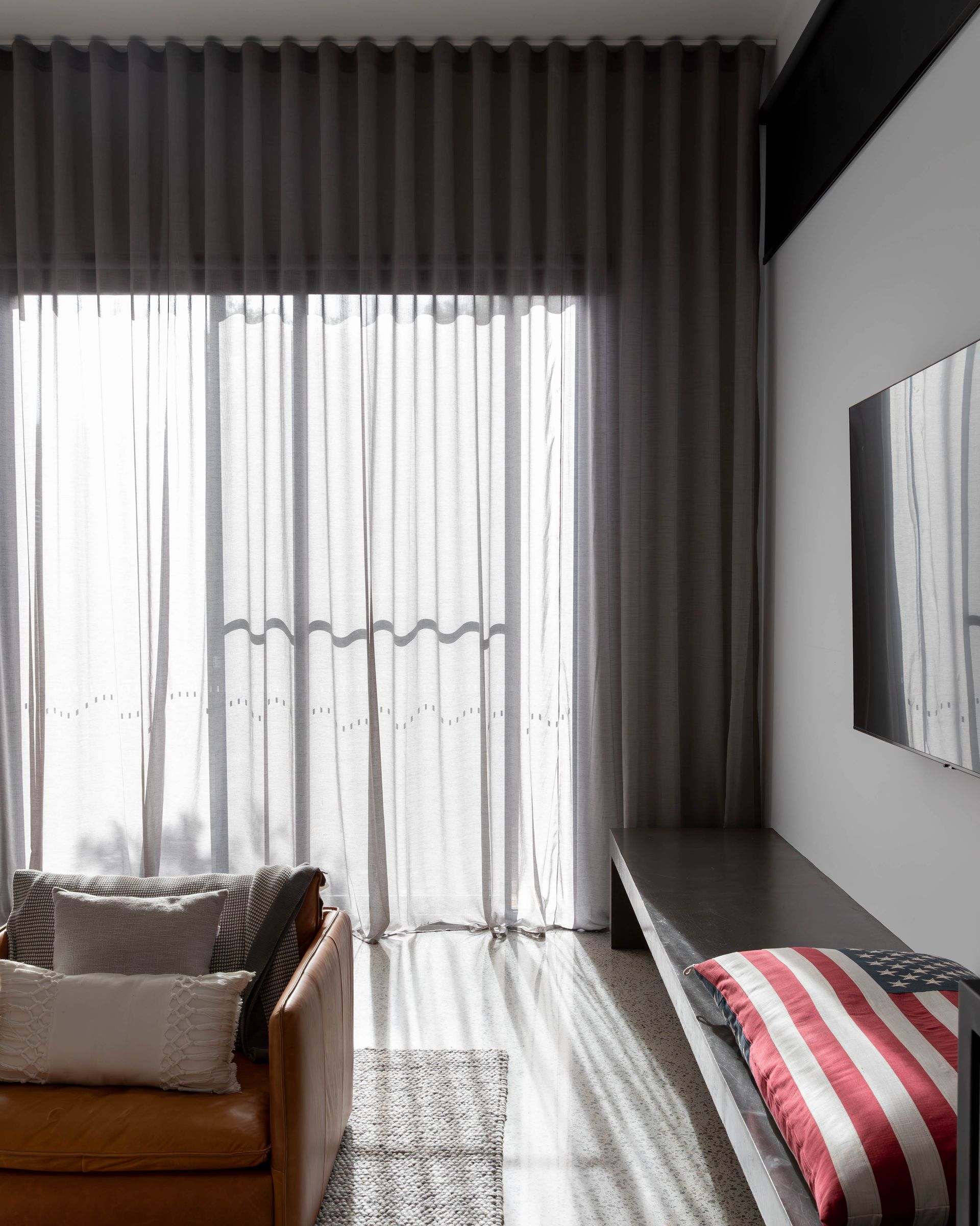 Bedroom with white shutters, round chandelier, and a blue bedspread. A chair sits to the left.