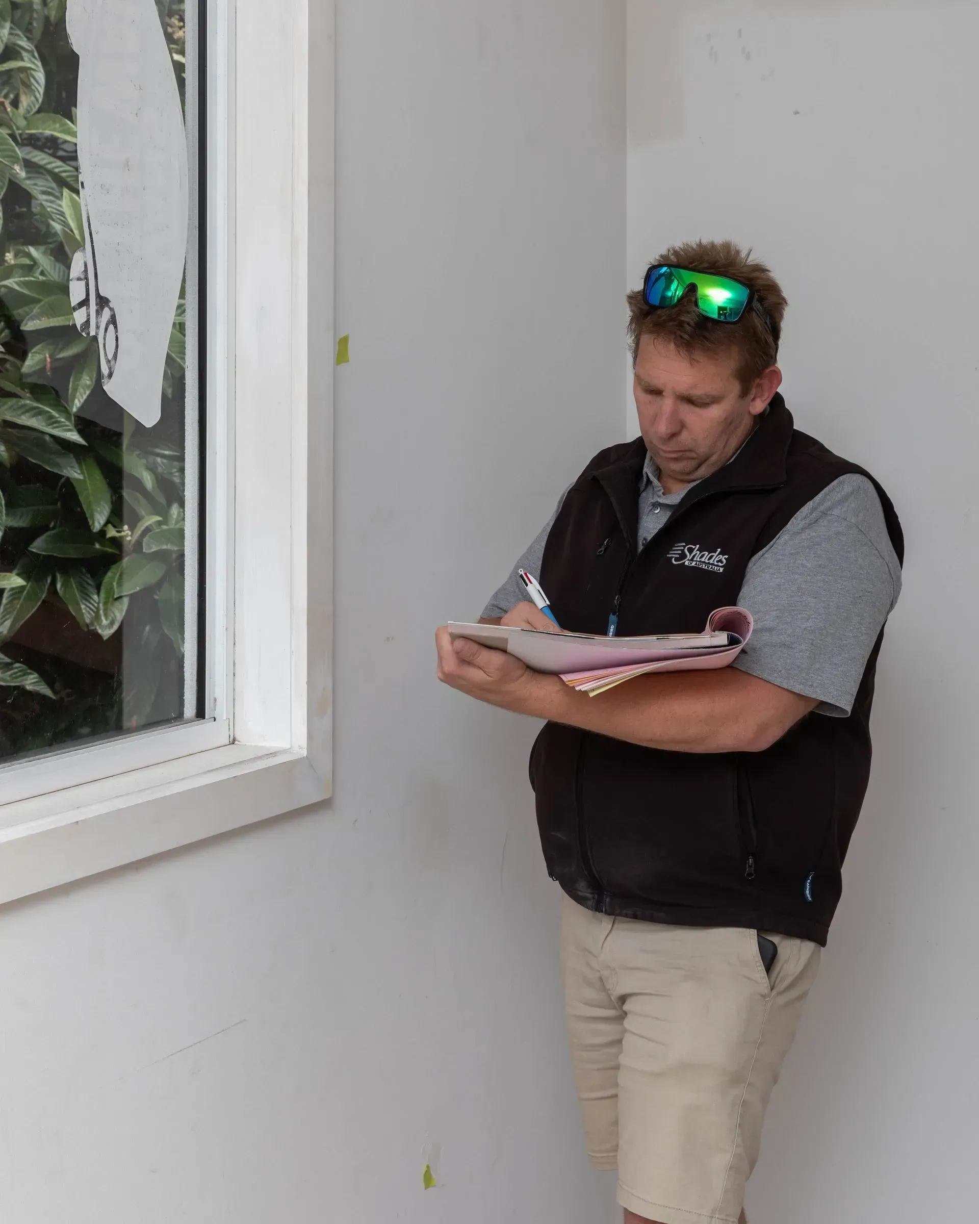 Man in vest looking at a notepad near a window. White walls.