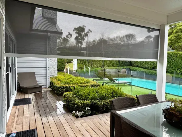 Outdoor patio with shade screen overlooking a garden and pool.