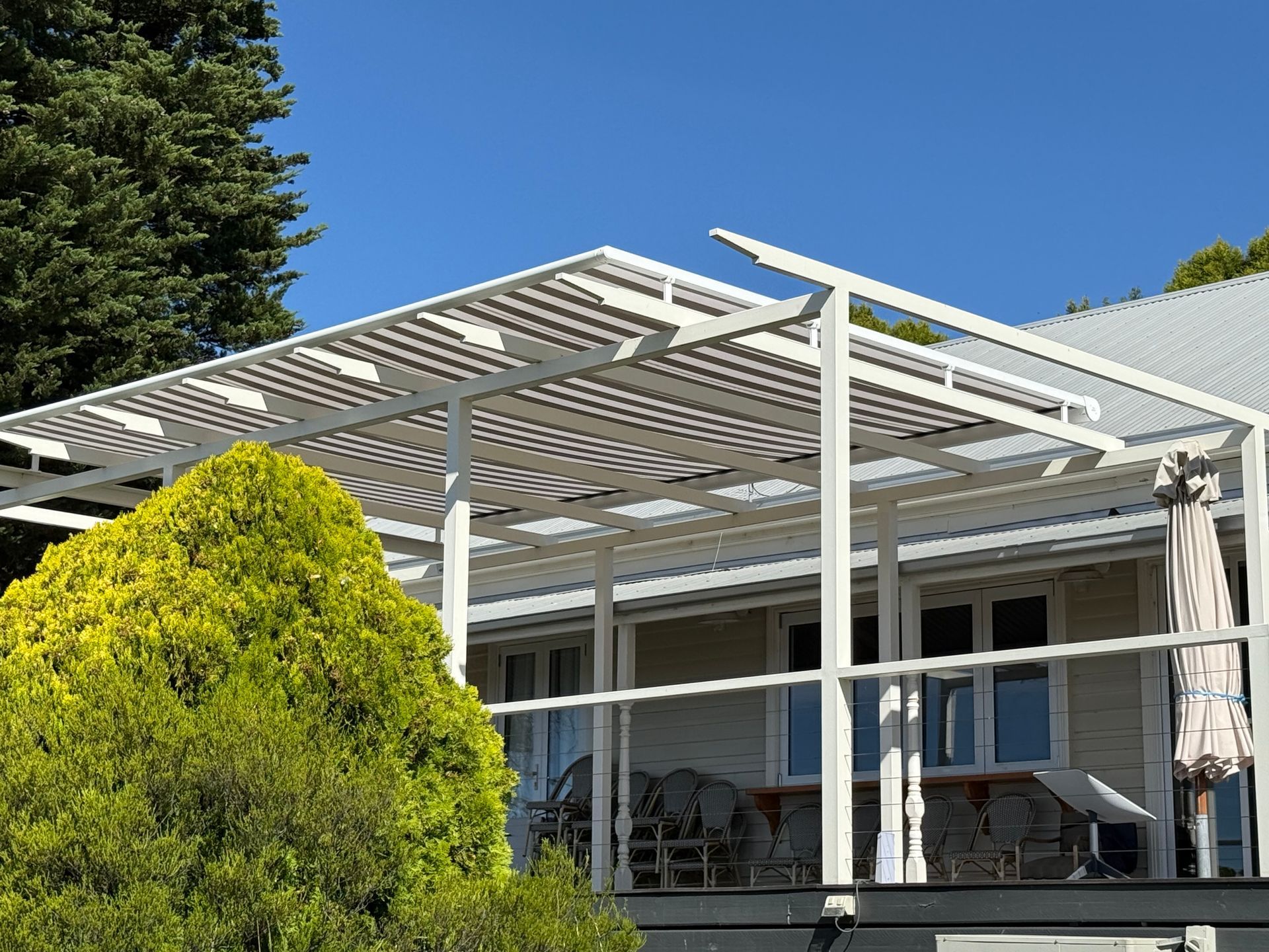 White pergola on a house deck with a slatted roof and clear blue sky.