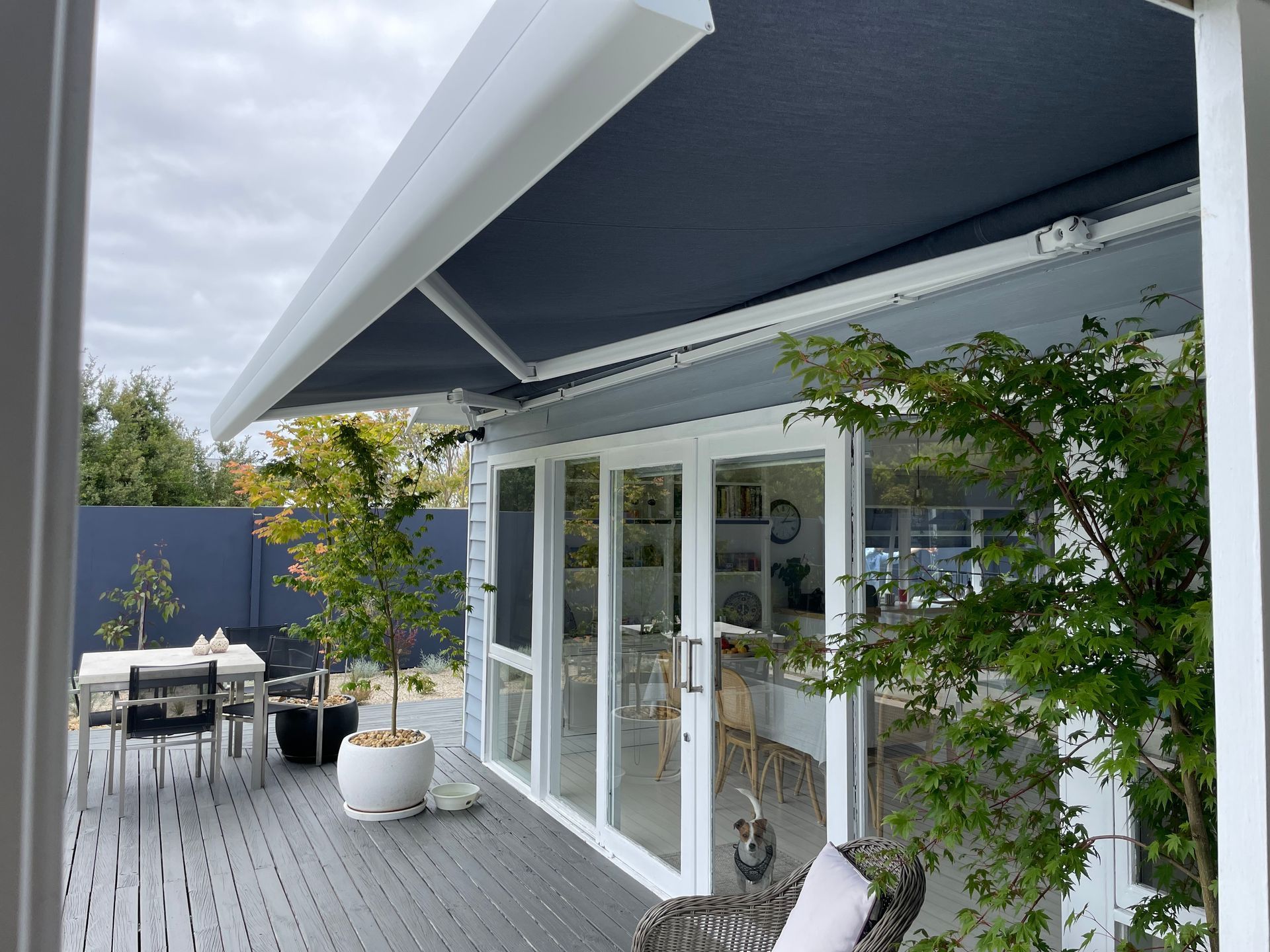 Deck with awning over French doors, table and chairs, and potted plants.
