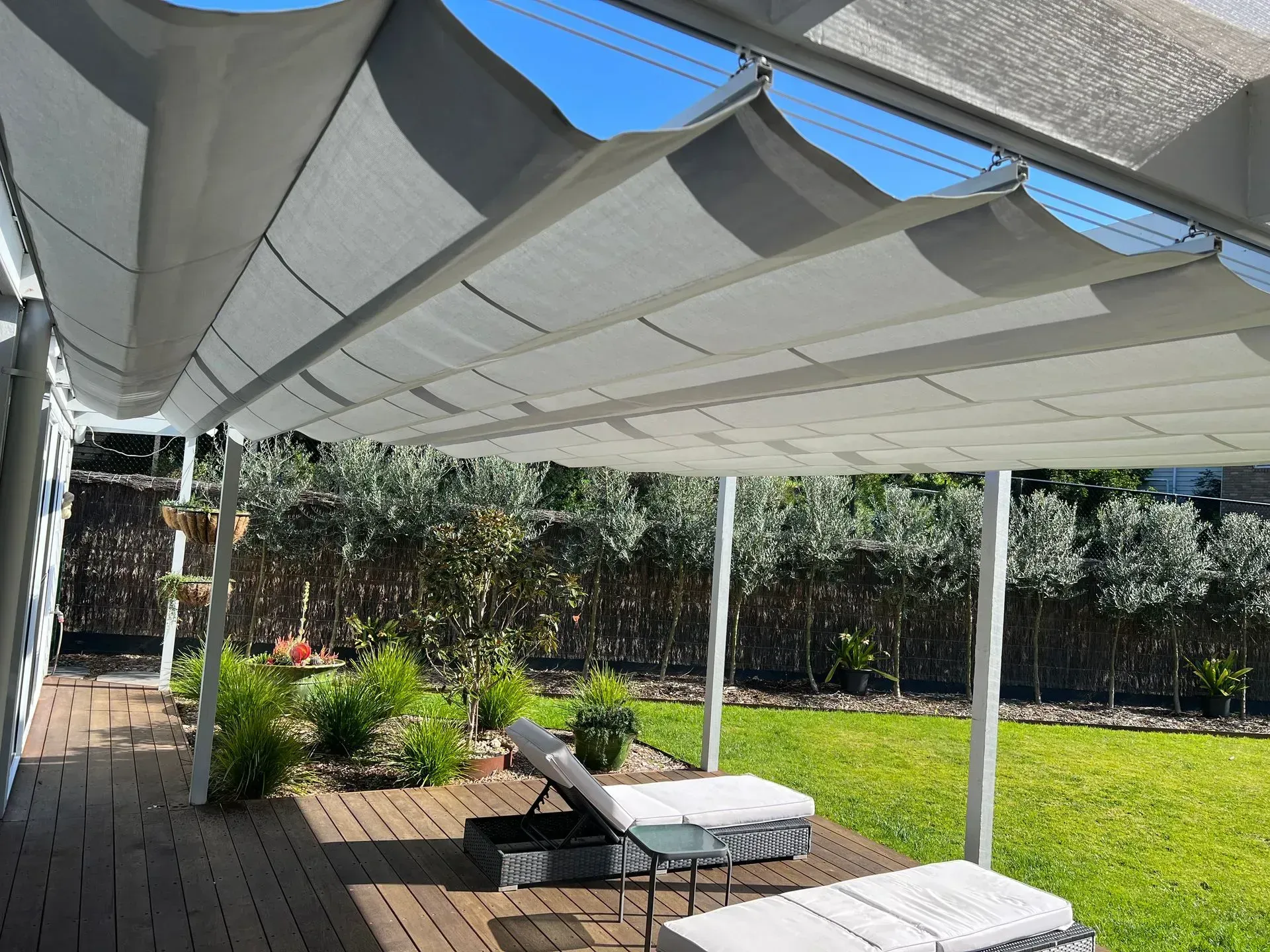 Deck with retractable canopy, lounge chairs, and garden in a sunny backyard.