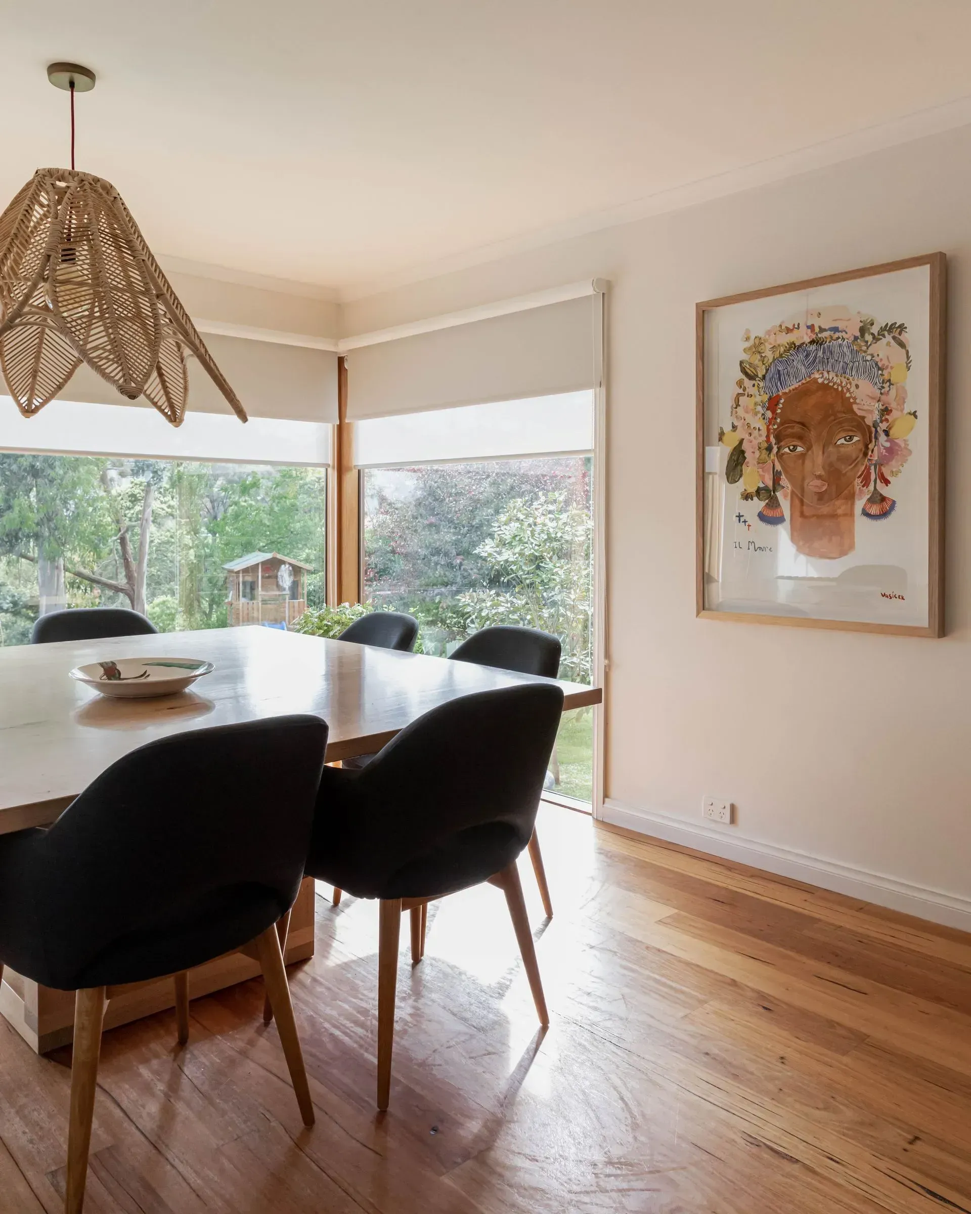 Dining room with wooden table, black chairs, artwork, and natural light.