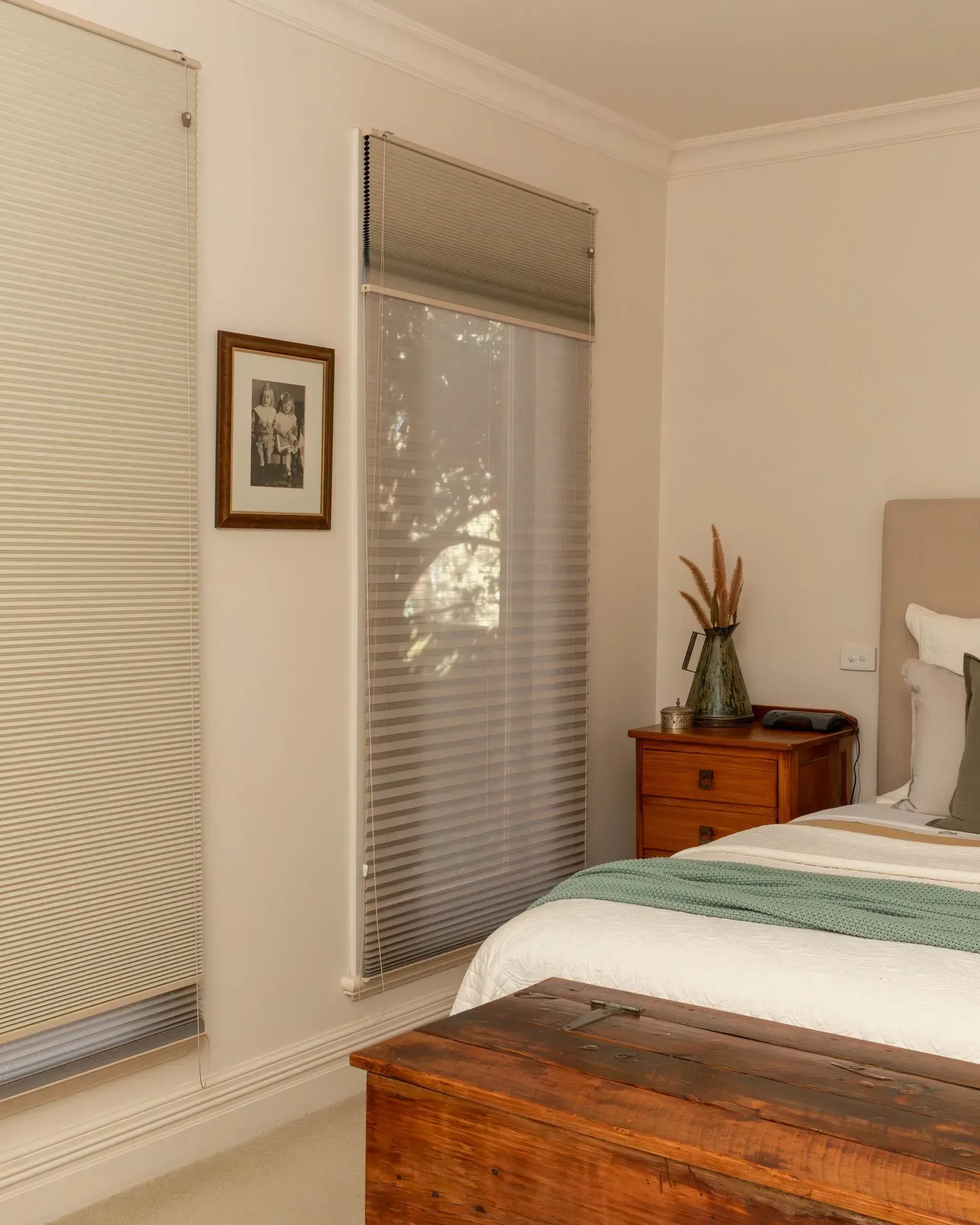 Bedroom interior with blinds, a bed, nightstand, and wooden chest.