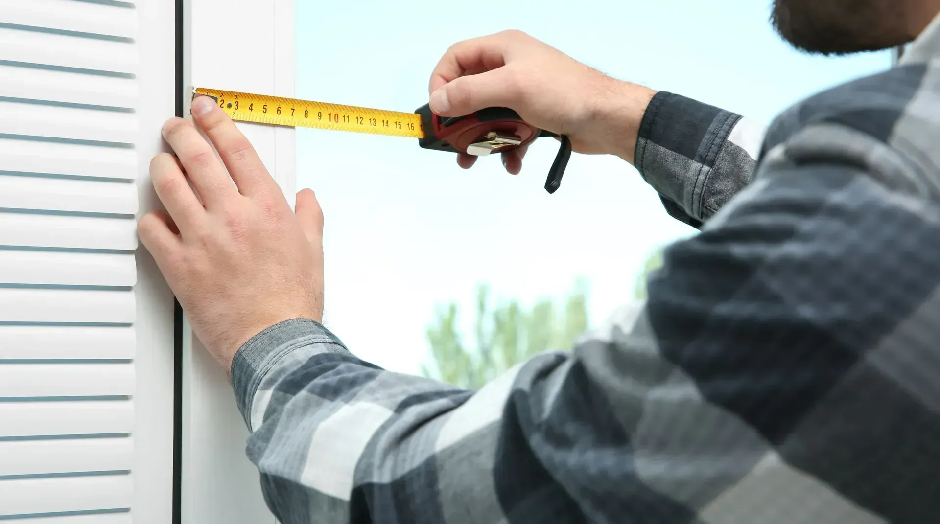 Person measuring a window frame with a yellow tape measure.