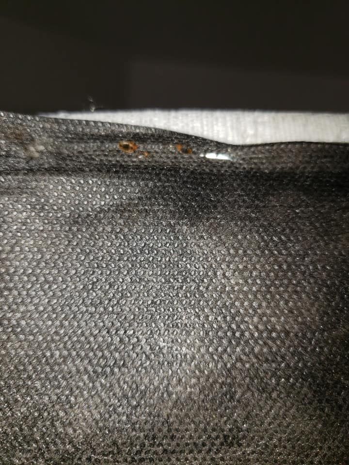 Close-up of a black woven fabric with small, dark brown or rust-colored spots on it.