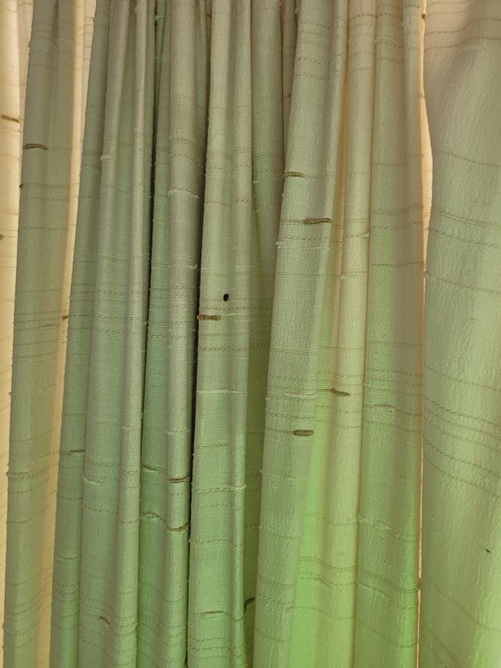 Close-up of vertical, off-white curtains with horizontal, thin, brown lines and subtle green gradient lighting.