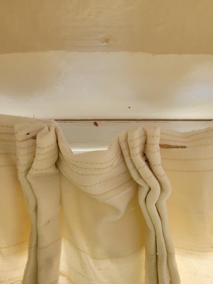Cream-colored curtains hanging from a white ledge with a few small dark spots visible.