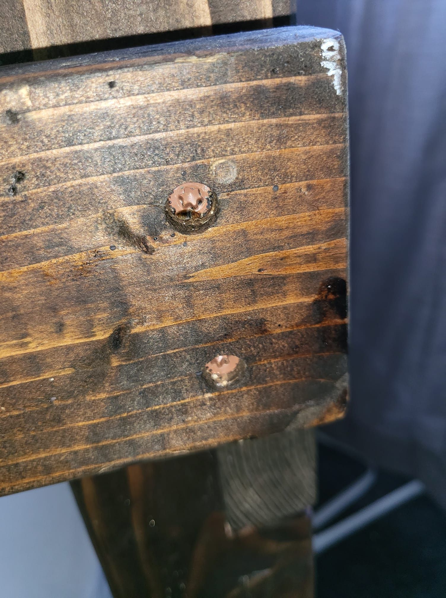 Close-up of a dark stained wooden beam with two rusty nails protruding from the surface.