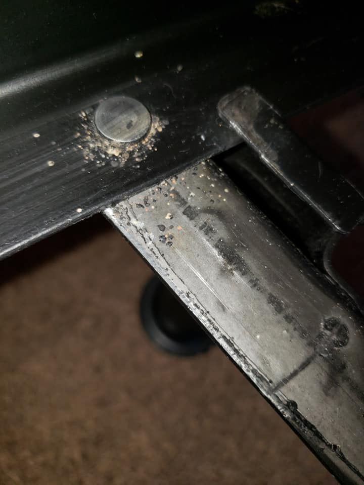 Close-up of a black metal joint with dust accumulation. A pin is visible near the joint, with a blurred dark background.